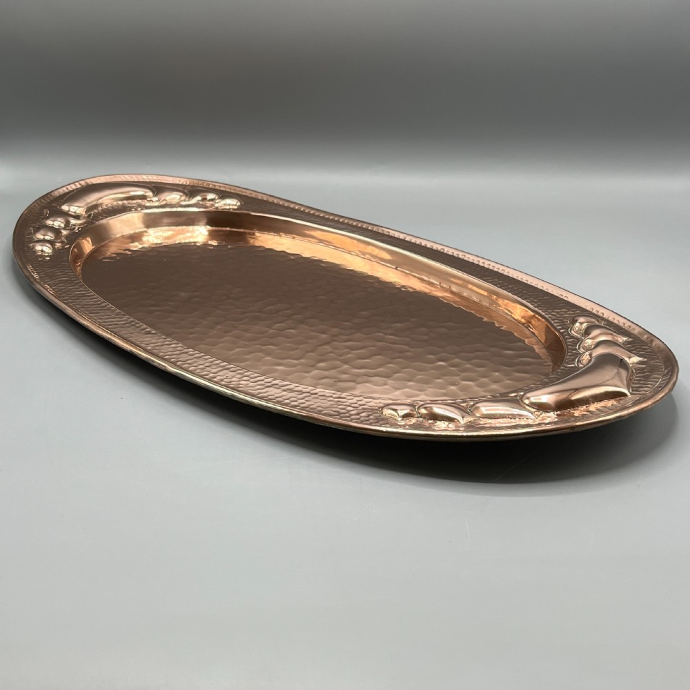 An oval Arts and Crafts copper tray featuring a planished hammered centre and stylised repousse detailing around the rim. View VII