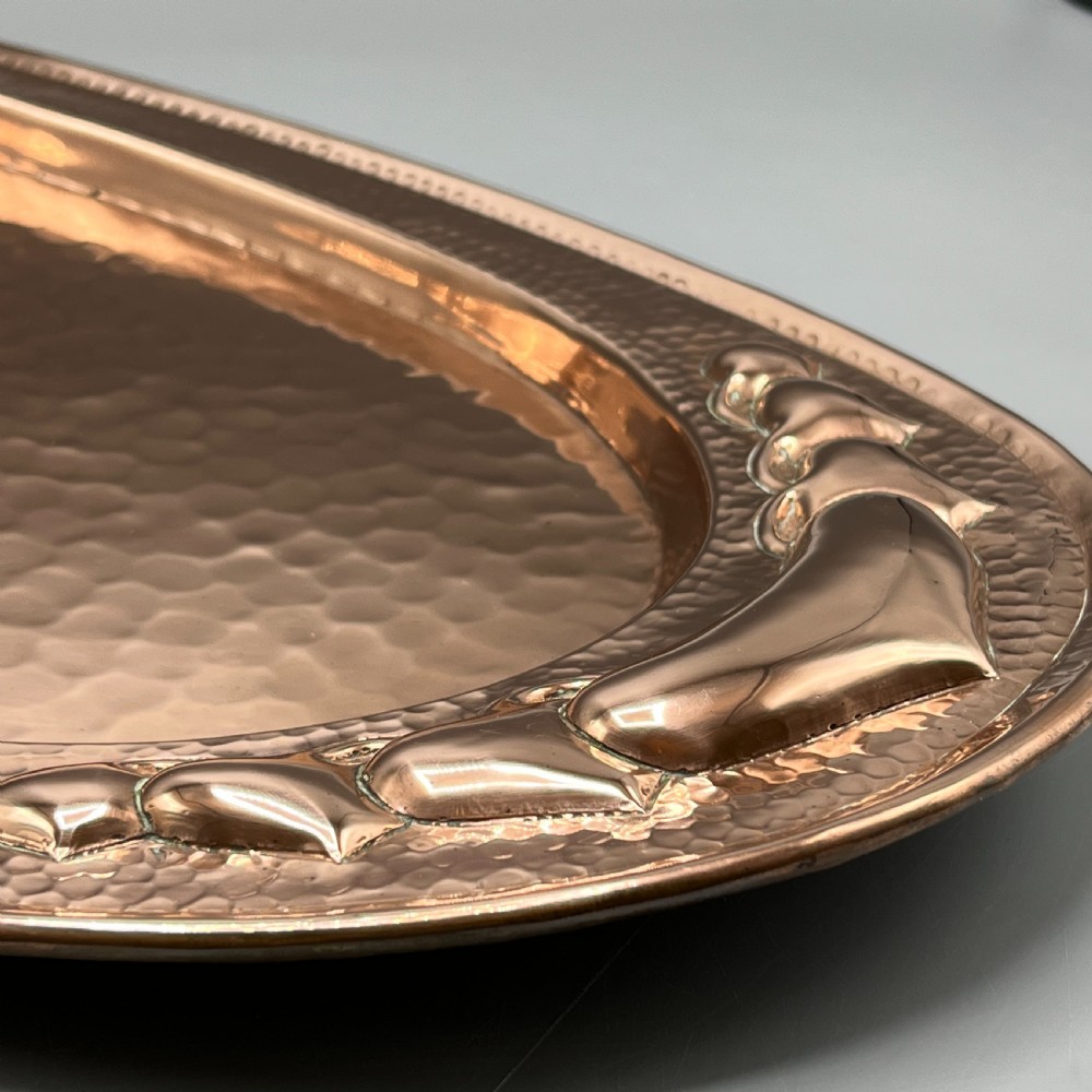 An oval Arts and Crafts copper tray featuring a planished hammered centre and stylised repousse detailing around the rim. View VIII