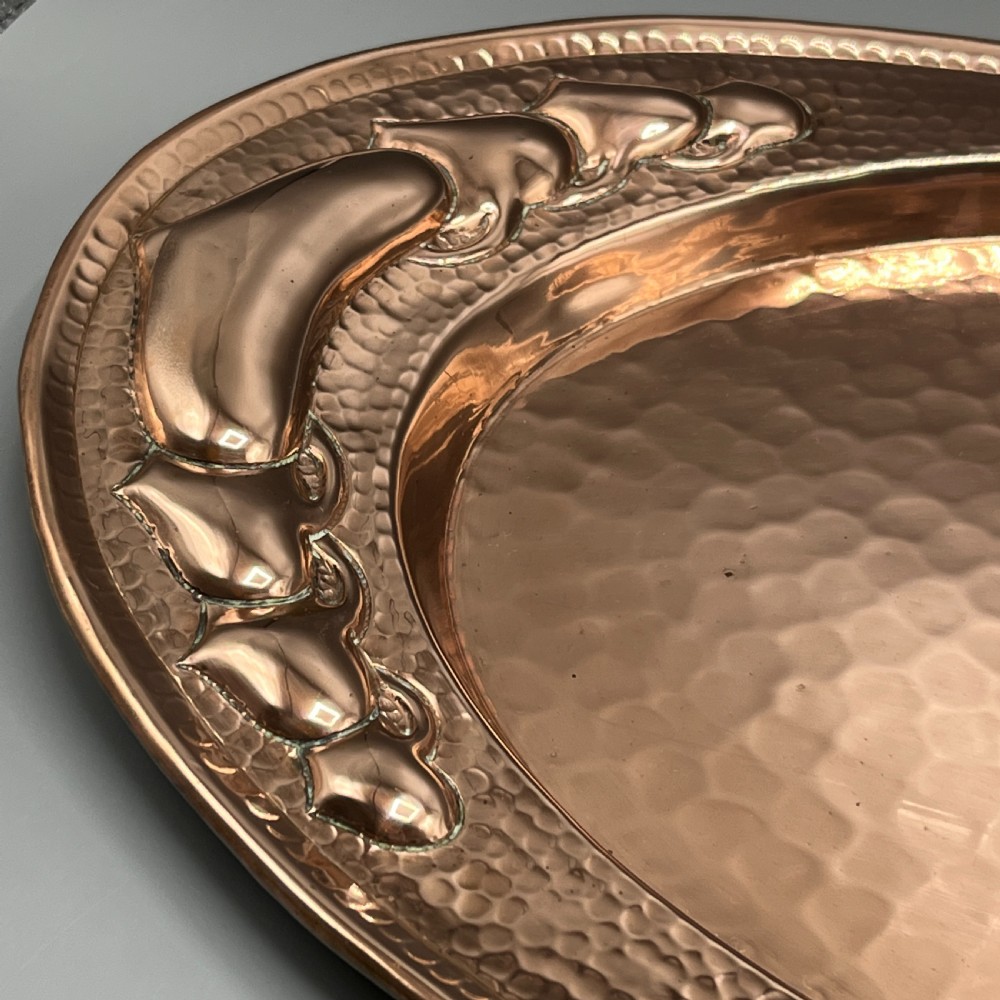 An oval Arts and Crafts copper tray featuring a planished hammered centre and stylised repousse detailing around the rim. View XI