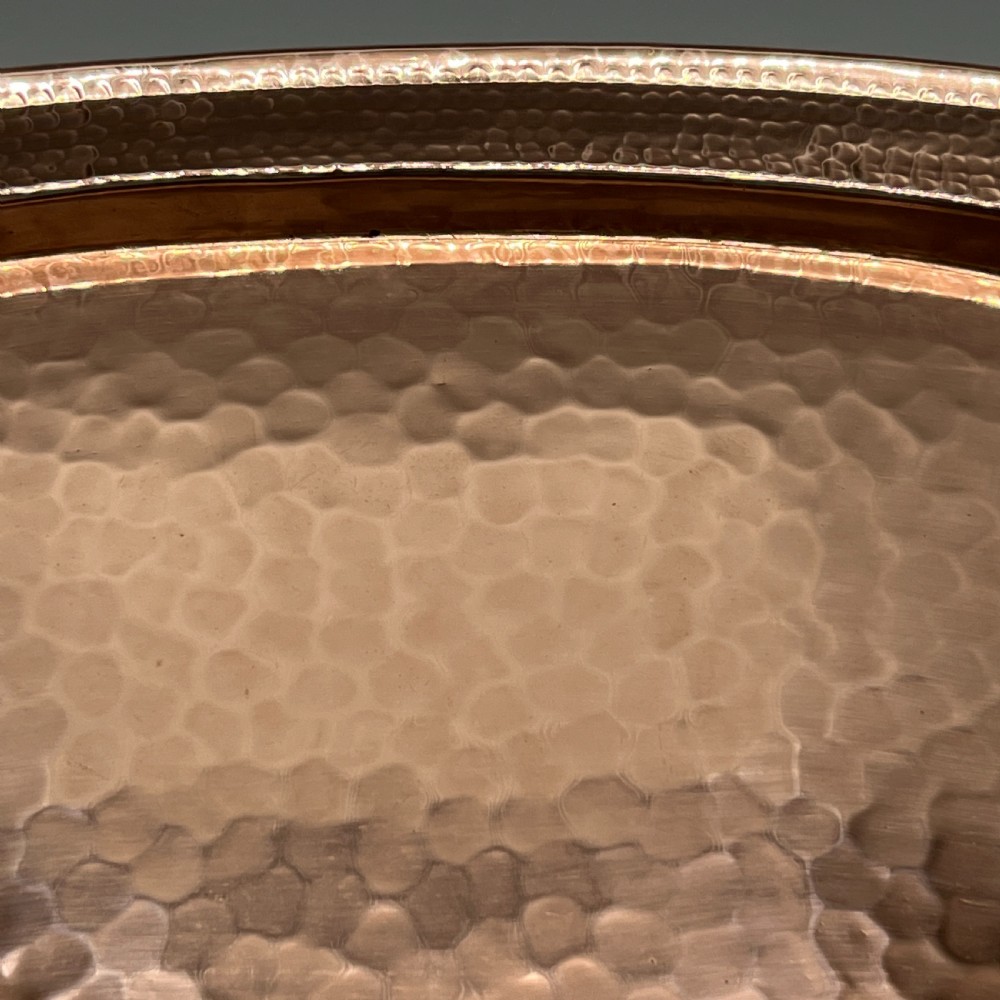 An oval Arts and Crafts copper tray featuring a planished hammered centre and stylised repousse detailing around the rim. View XIII