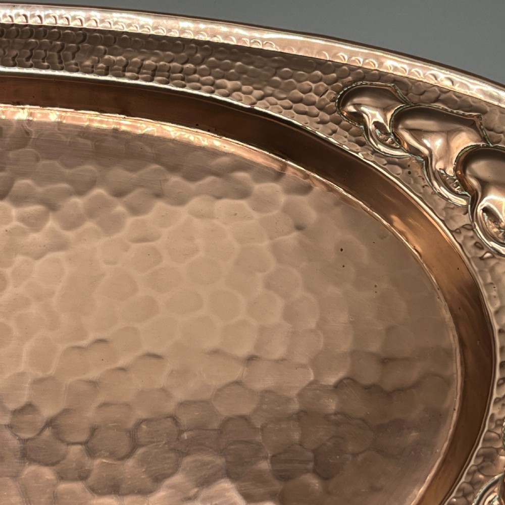 An oval Arts and Crafts copper tray featuring a planished hammered centre and stylised repousse detailing around the rim. View XIV
