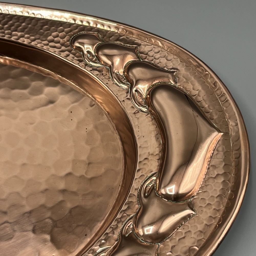 An oval Arts and Crafts copper tray featuring a planished hammered centre and stylised repousse detailing around the rim. View XV
