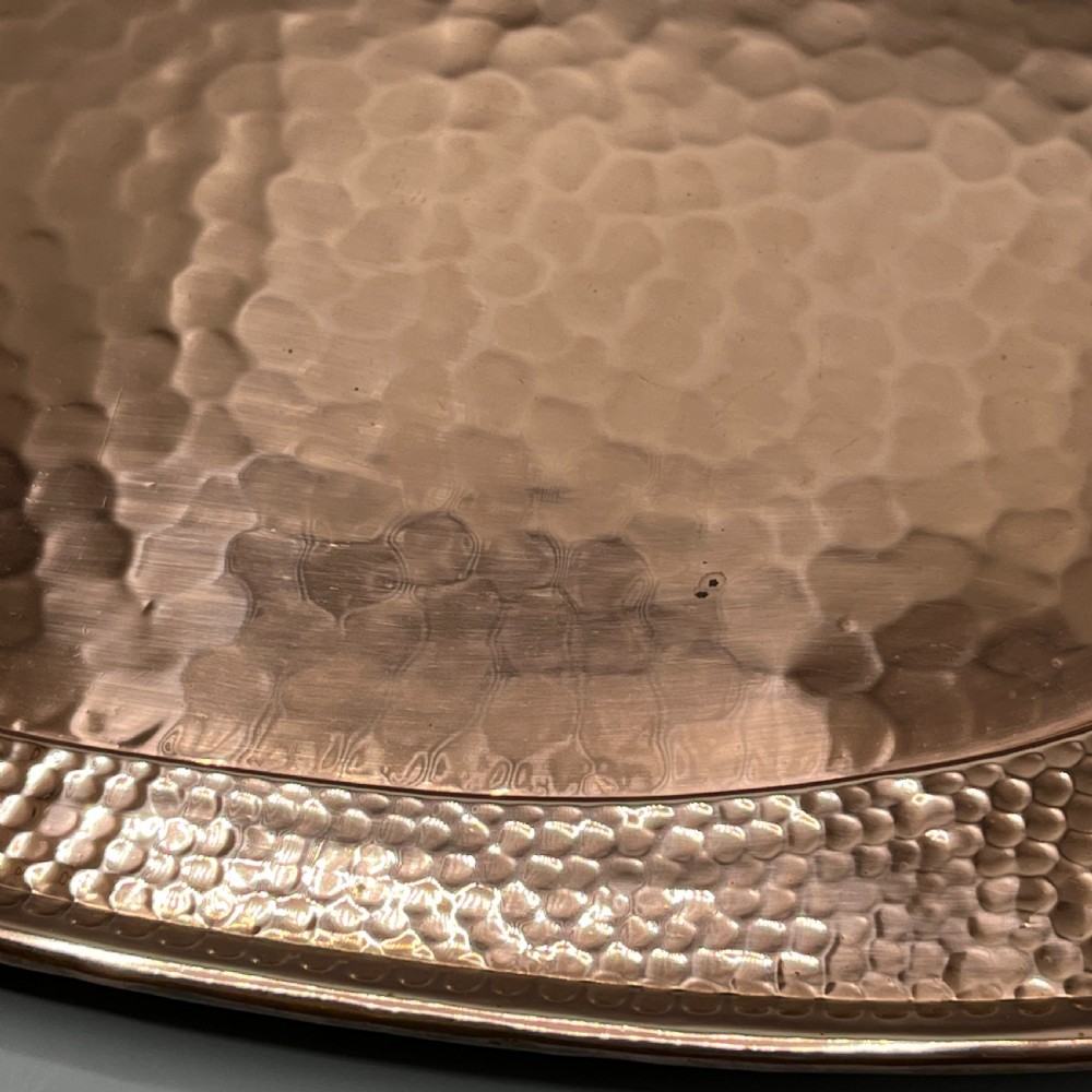 An oval Arts and Crafts copper tray featuring a planished hammered centre and stylised repousse detailing around the rim. View XVII