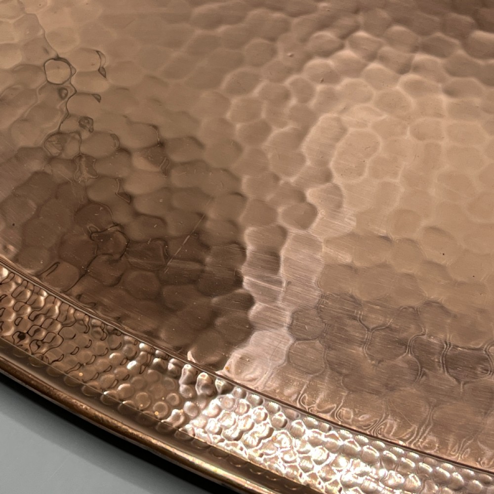 An oval Arts and Crafts copper tray featuring a planished hammered centre and stylised repousse detailing around the rim. View XVIII