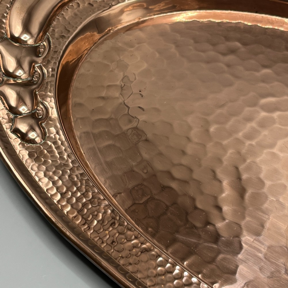 An oval Arts and Crafts copper tray featuring a planished hammered centre and stylised repousse detailing around the rim. View XIX