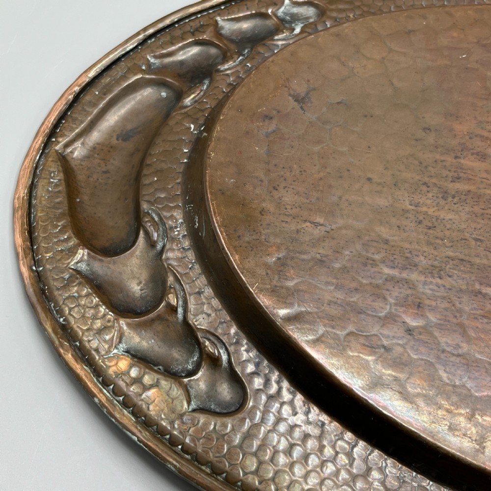 An oval Arts and Crafts copper tray featuring a planished hammered centre and stylised repousse detailing around the rim. View XXI