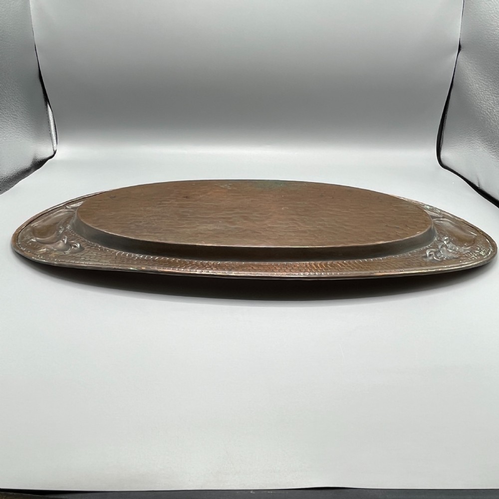An oval Arts and Crafts copper tray featuring a planished hammered centre and stylised repousse detailing around the rim. View XXII