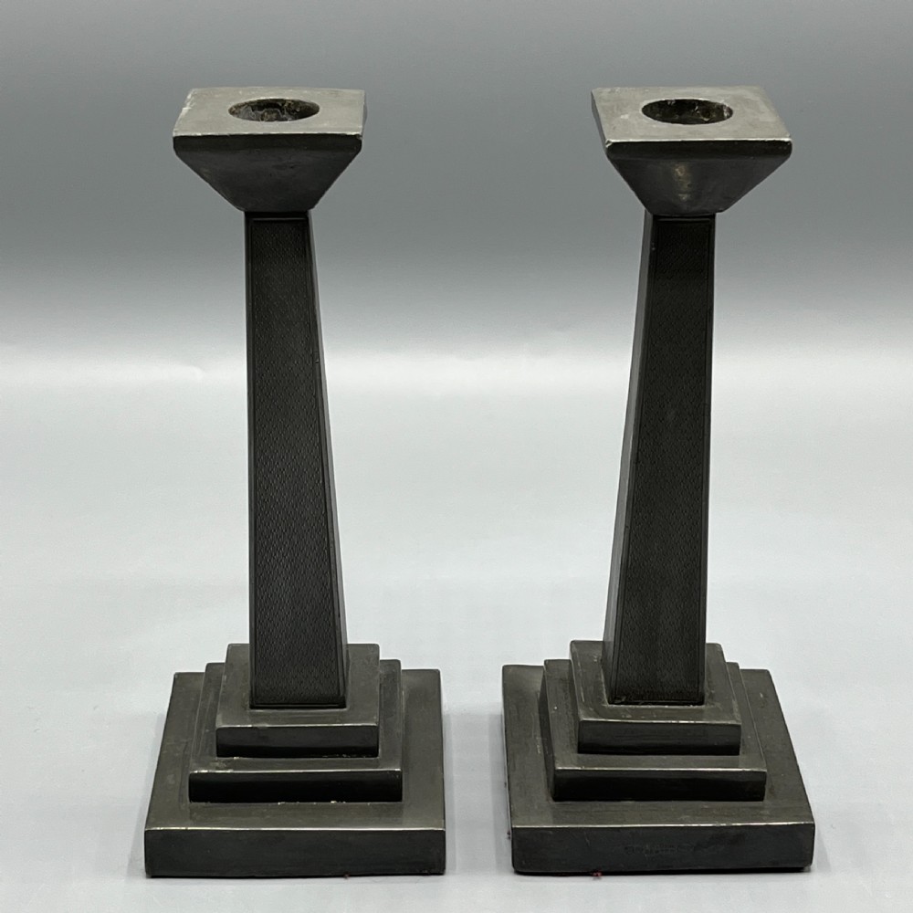 A pair of dark grey Art Deco pewter candlesticks featuring stepped square bases and tapered central columns.