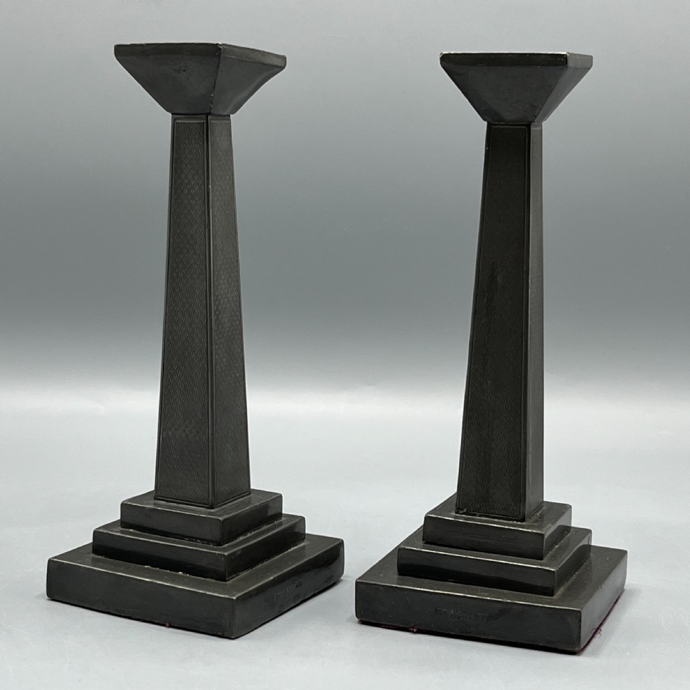A pair of dark grey Art Deco pewter candlesticks featuring stepped square bases and tapered central columns. View V