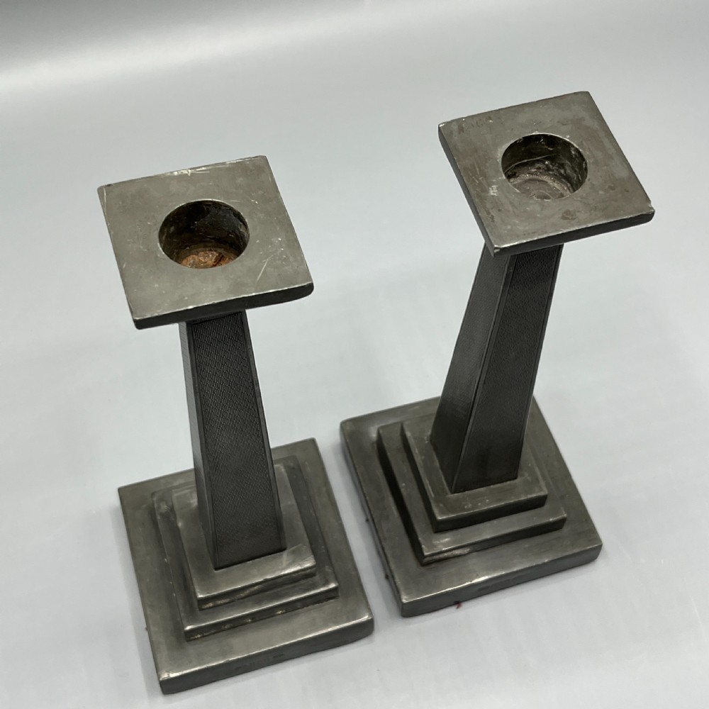 A pair of dark grey Art Deco pewter candlesticks featuring stepped square bases and tapered central columns. View IX