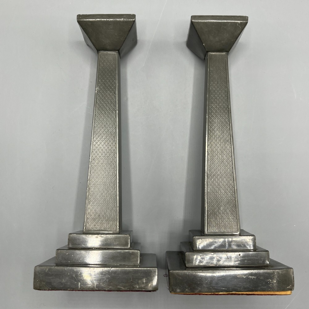 A pair of dark grey Art Deco pewter candlesticks featuring stepped square bases and tapered central columns. View XV