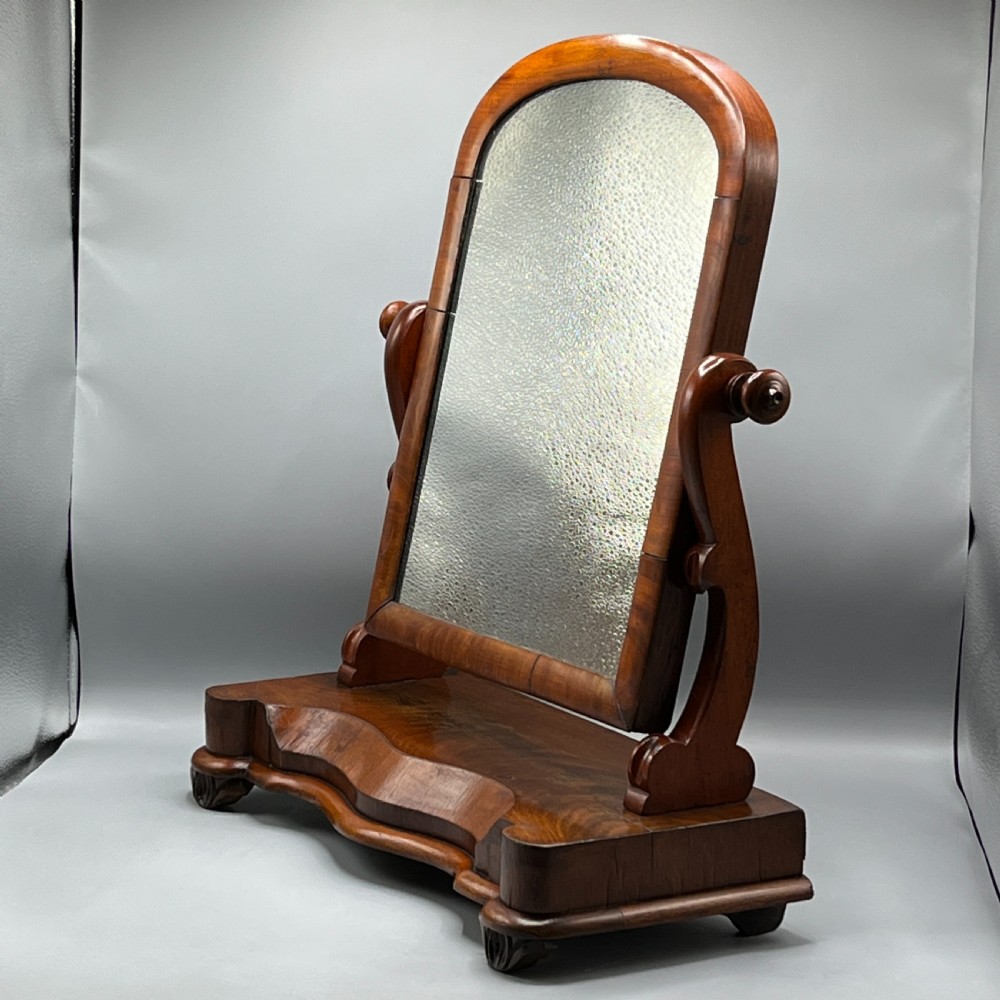 A Victorian mahogany dressing table mirror with an arched swivel frame and carved scroll uprights set on a serpentine base. View II