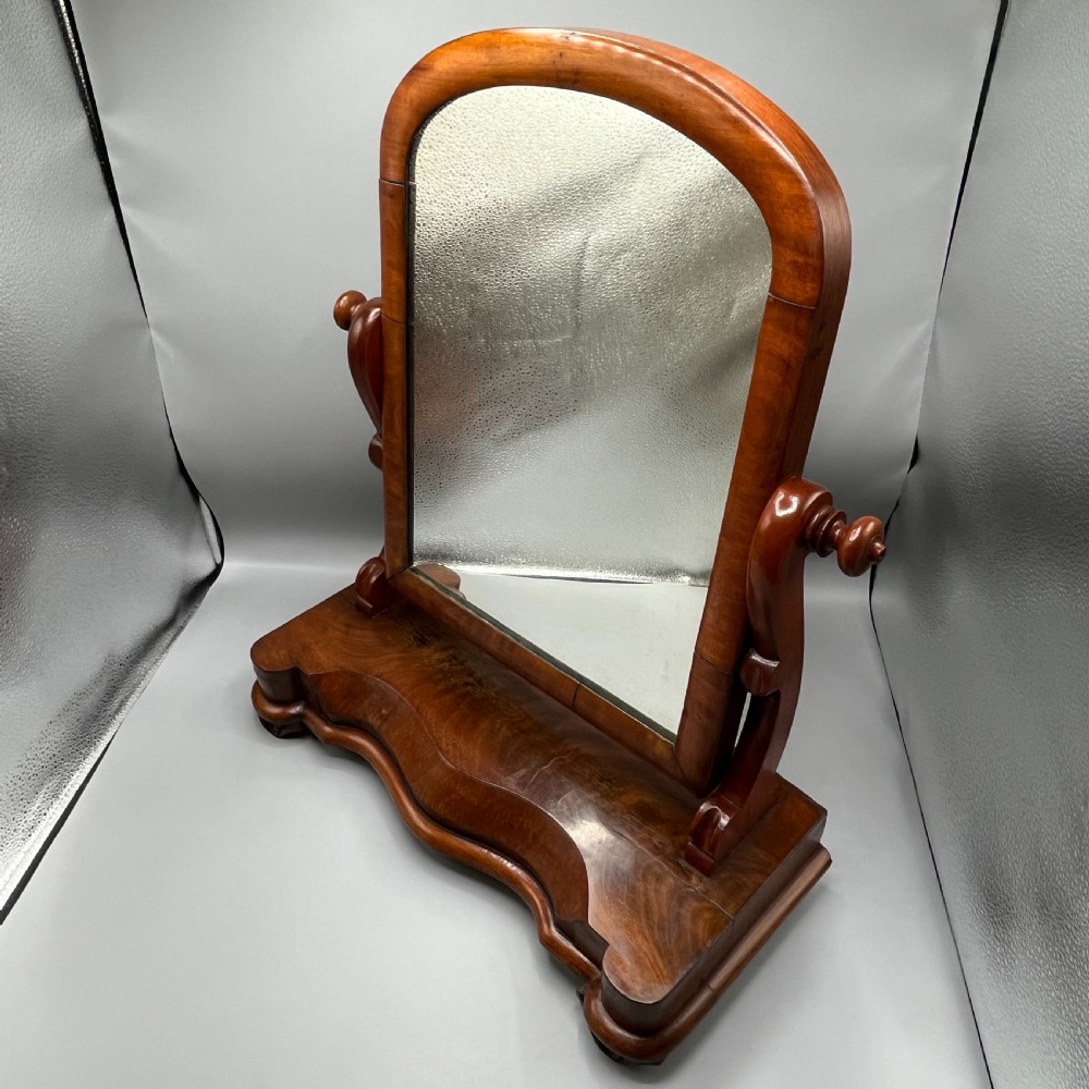 A Victorian mahogany dressing table mirror with an arched swivel frame and carved scroll uprights set on a serpentine base. View III