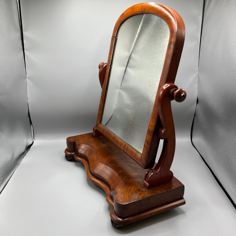 A Victorian mahogany dressing table mirror with an arched swivel frame and carved scroll uprights set on a serpentine base. View IV