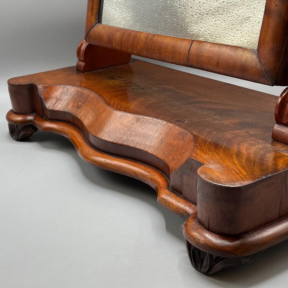 A Victorian mahogany dressing table mirror with an arched swivel frame and carved scroll uprights set on a serpentine base. View VI