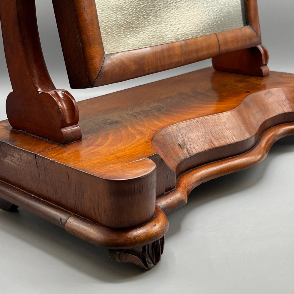A Victorian mahogany dressing table mirror with an arched swivel frame and carved scroll uprights set on a serpentine base. View VII