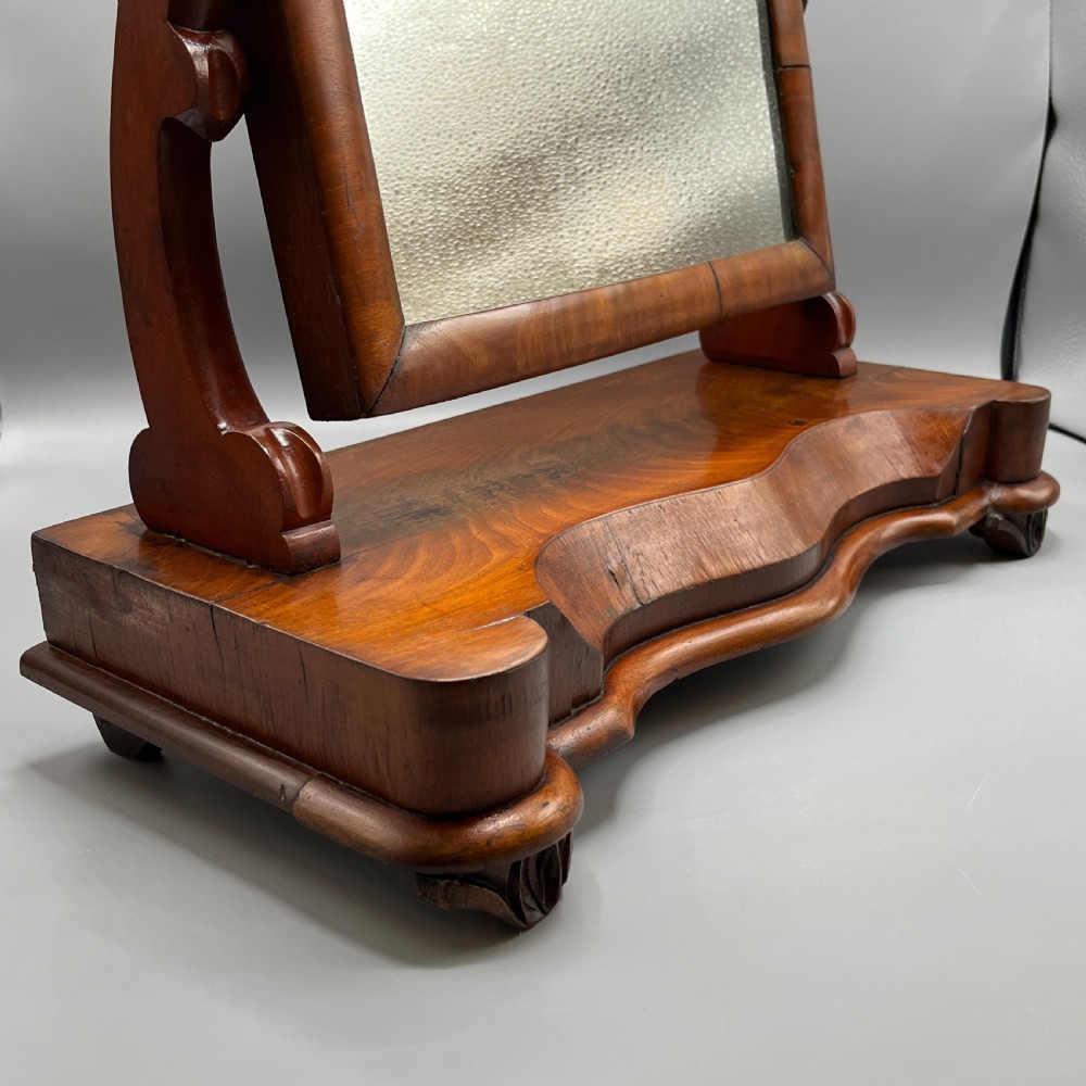 A Victorian mahogany dressing table mirror with an arched swivel frame and carved scroll uprights set on a serpentine base. View VIII