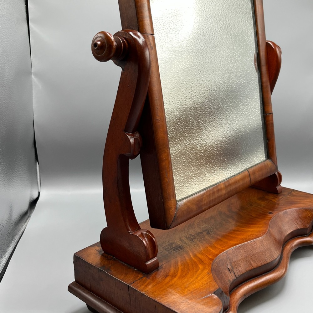 A Victorian mahogany dressing table mirror with an arched swivel frame and carved scroll uprights set on a serpentine base. View IX