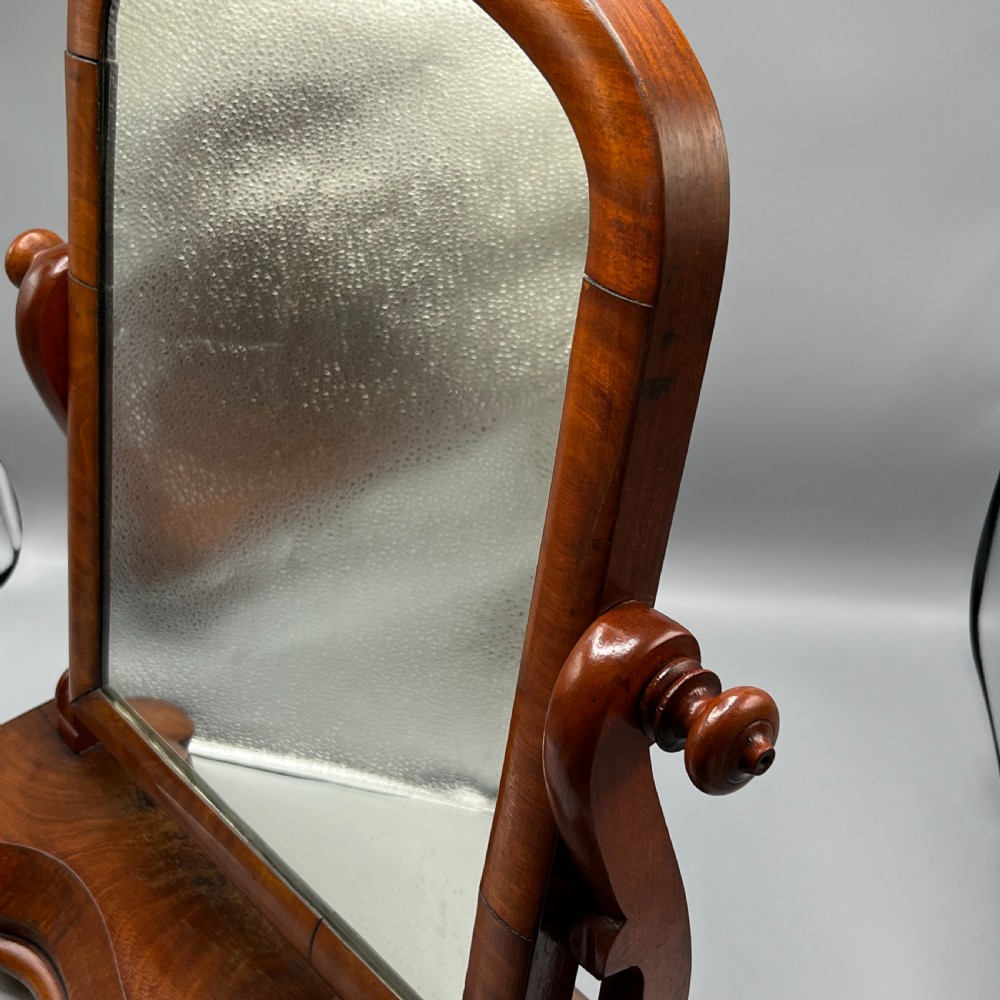 A Victorian mahogany dressing table mirror with an arched swivel frame and carved scroll uprights set on a serpentine base. View XXI