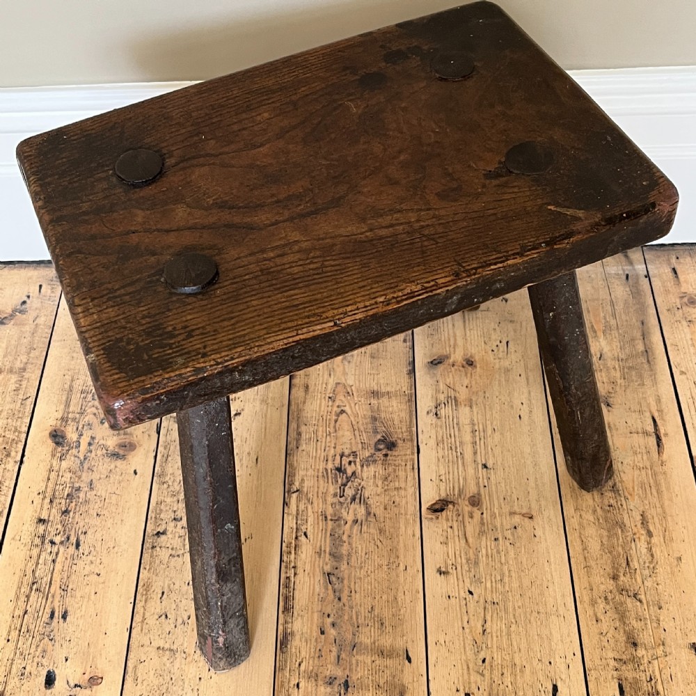 A rustic dark oak four-legged stool featuring a thick rectangular top with four visible circular wedged tenons and splayed faceted legs. View IV