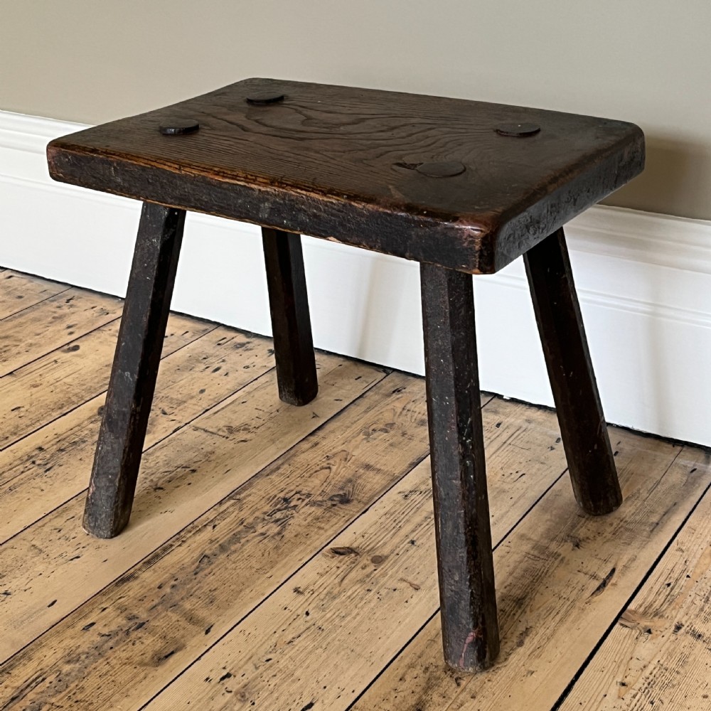 A rustic dark oak four-legged stool featuring a thick rectangular top with four visible circular wedged tenons and splayed faceted legs. View VIII