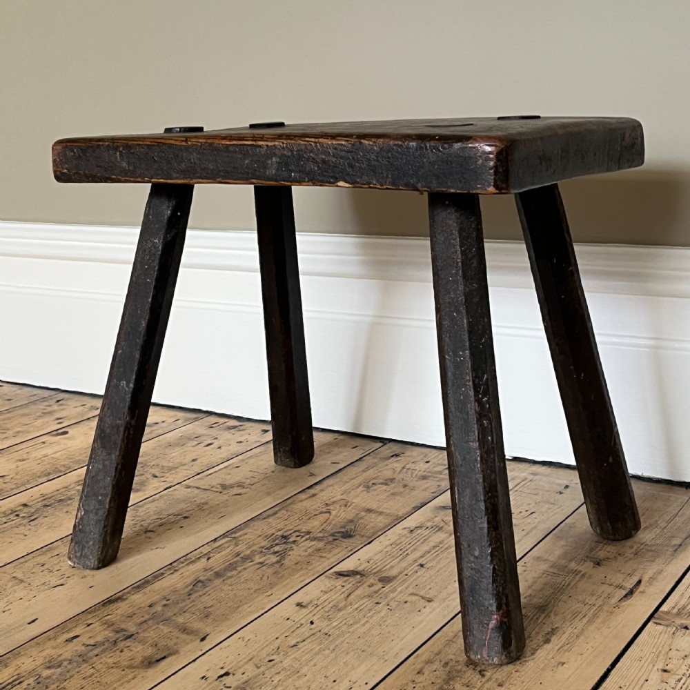 A rustic dark oak four-legged stool featuring a thick rectangular top with four visible circular wedged tenons and splayed faceted legs. View IX