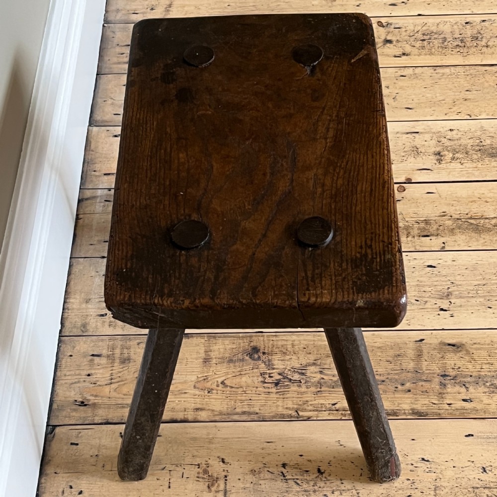 A rustic dark oak four-legged stool featuring a thick rectangular top with four visible circular wedged tenons and splayed faceted legs. View XI