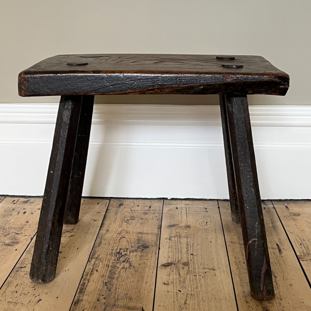 A rustic dark oak four-legged stool featuring a thick rectangular top with four visible circular wedged tenons and splayed faceted legs. View XII