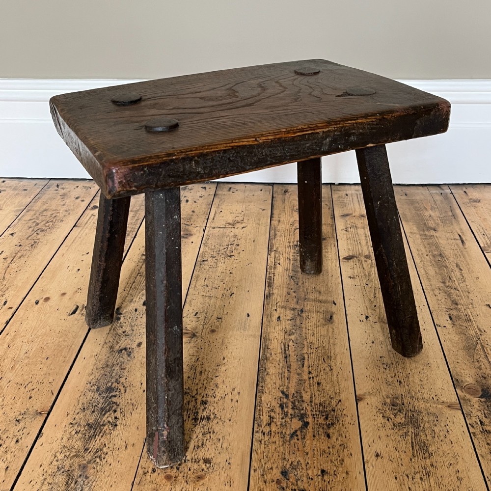 A rustic dark oak four-legged stool featuring a thick rectangular top with four visible circular wedged tenons and splayed faceted legs. View XV