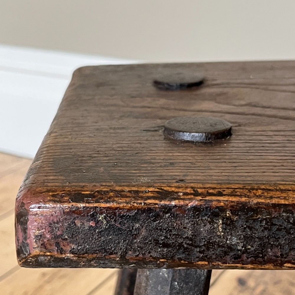 A rustic dark oak four-legged stool featuring a thick rectangular top with four visible circular wedged tenons and splayed faceted legs. View XVI