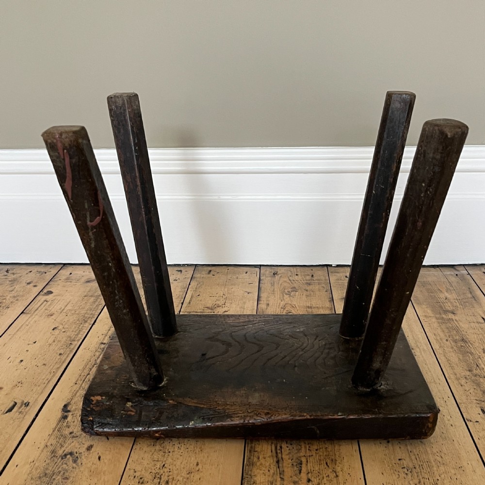 A rustic dark oak four-legged stool featuring a thick rectangular top with four visible circular wedged tenons and splayed faceted legs. View XVIII