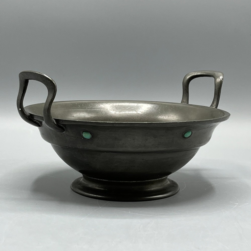 An Arts and Crafts pewter porringer bowl featuring twin raised handles, a pedestal base, and small turquoise cabochons set into the exterior rim.