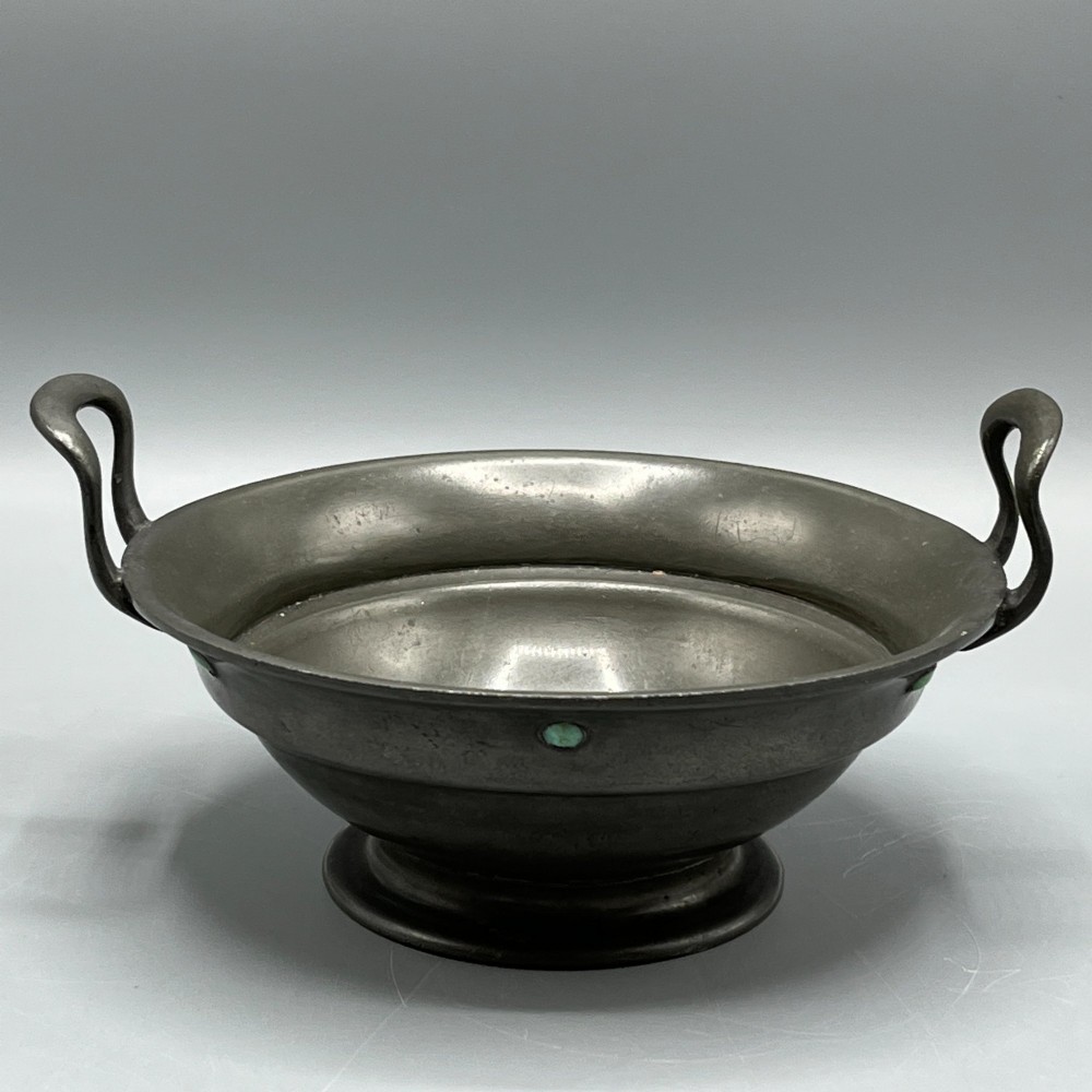 An Arts and Crafts pewter porringer bowl featuring twin raised handles, a pedestal base, and small turquoise cabochons set into the exterior rim. View VI