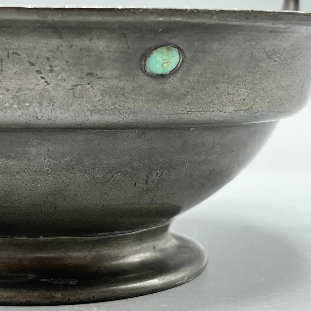 An Arts and Crafts pewter porringer bowl featuring twin raised handles, a pedestal base, and small turquoise cabochons set into the exterior rim. View IX
