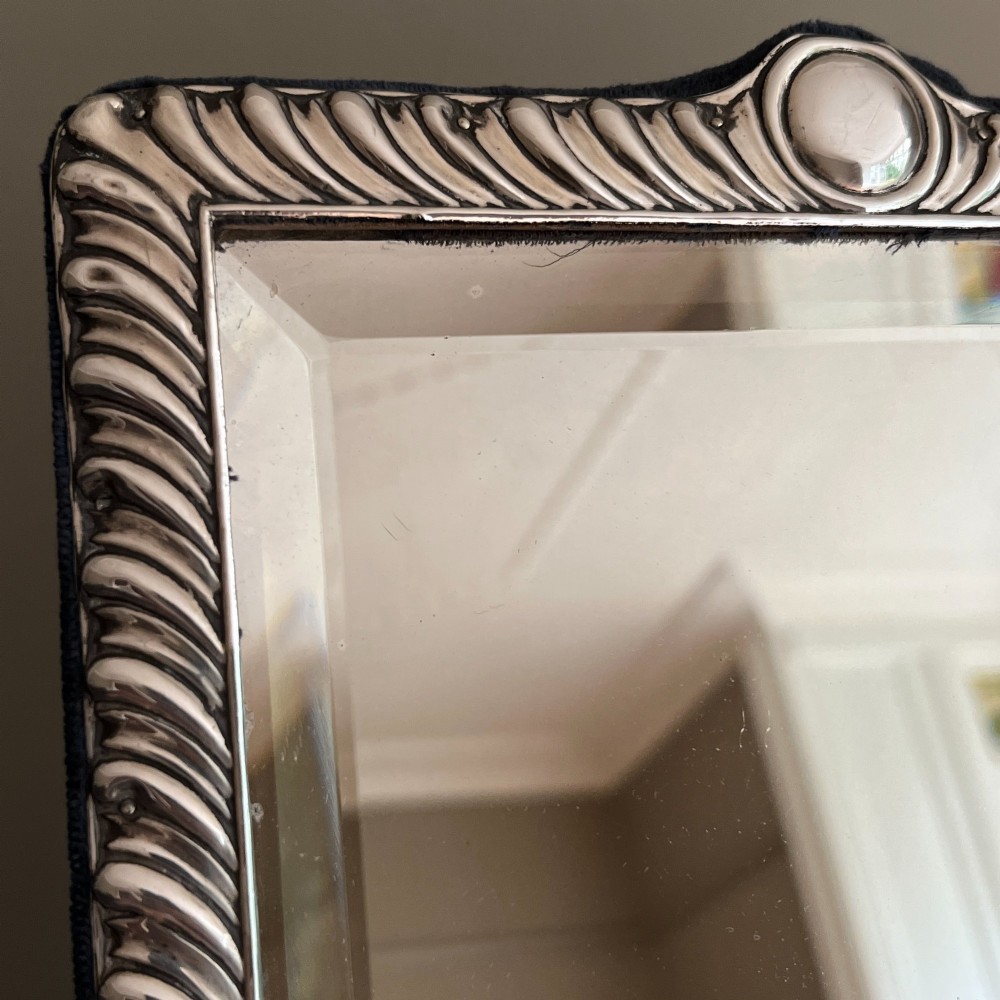An Edwardian rectangular sterling silver strut mirror featuring a fluted gadrooned frame, a central circular boss crest, and bevelled mirror glass. View III