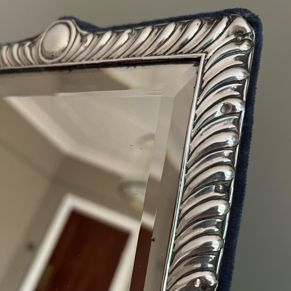 An Edwardian rectangular sterling silver strut mirror featuring a fluted gadrooned frame, a central circular boss crest, and bevelled mirror glass. View IV