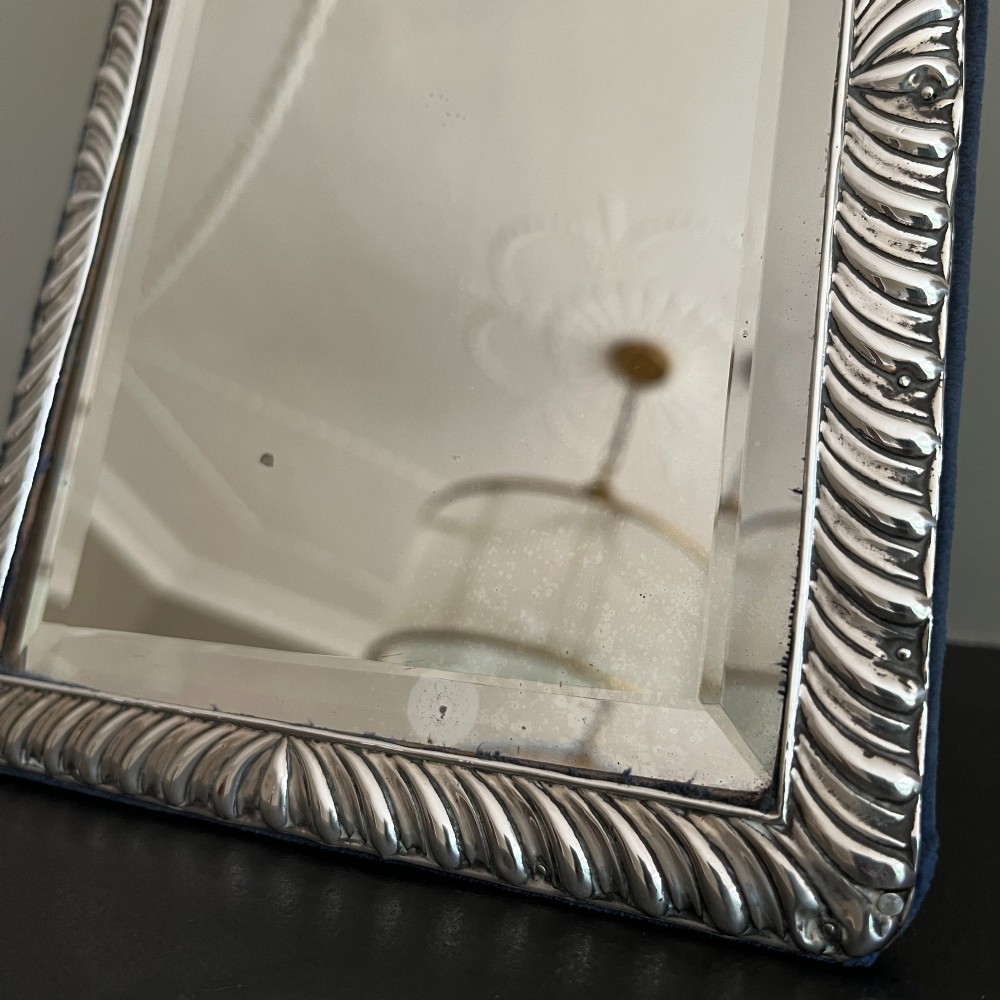 An Edwardian rectangular sterling silver strut mirror featuring a fluted gadrooned frame, a central circular boss crest, and bevelled mirror glass. View VI