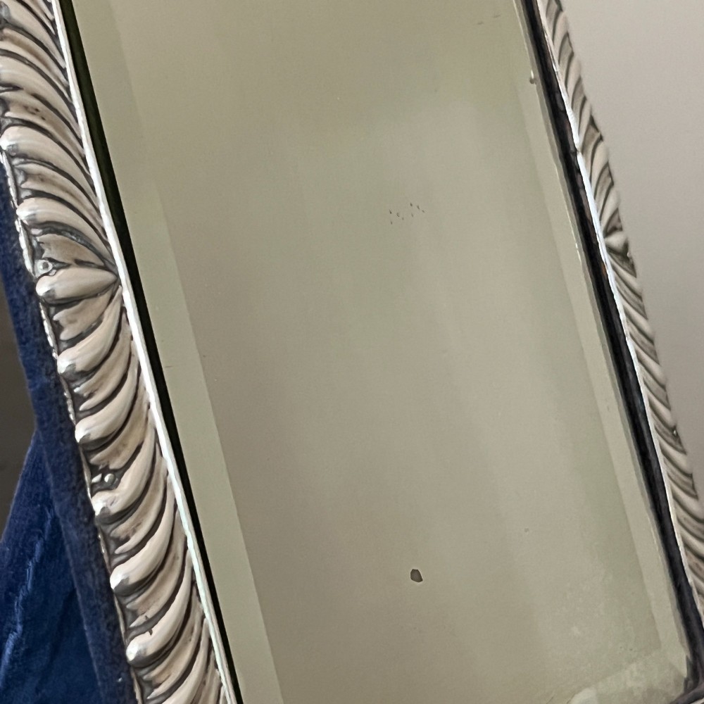 An Edwardian rectangular sterling silver strut mirror featuring a fluted gadrooned frame, a central circular boss crest, and bevelled mirror glass. View VIII