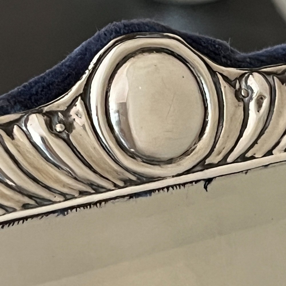 An Edwardian rectangular sterling silver strut mirror featuring a fluted gadrooned frame, a central circular boss crest, and bevelled mirror glass. View X