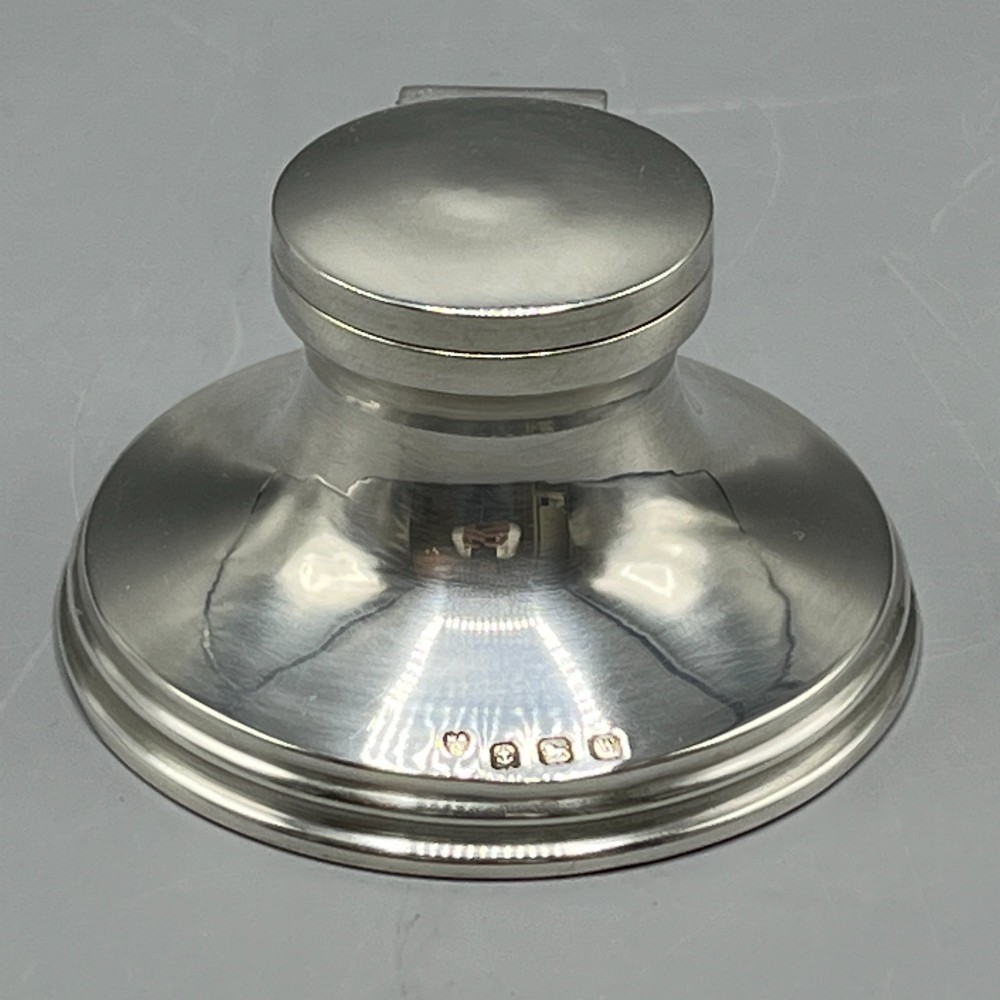 An Art Deco sterling silver capstan inkwell featuring a smooth hinged lid, circular stepped base, and visible hallmarks.