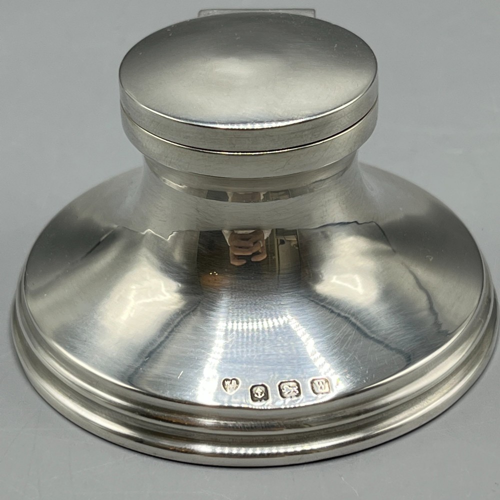 An Art Deco sterling silver capstan inkwell featuring a smooth hinged lid, circular stepped base, and visible hallmarks. View V