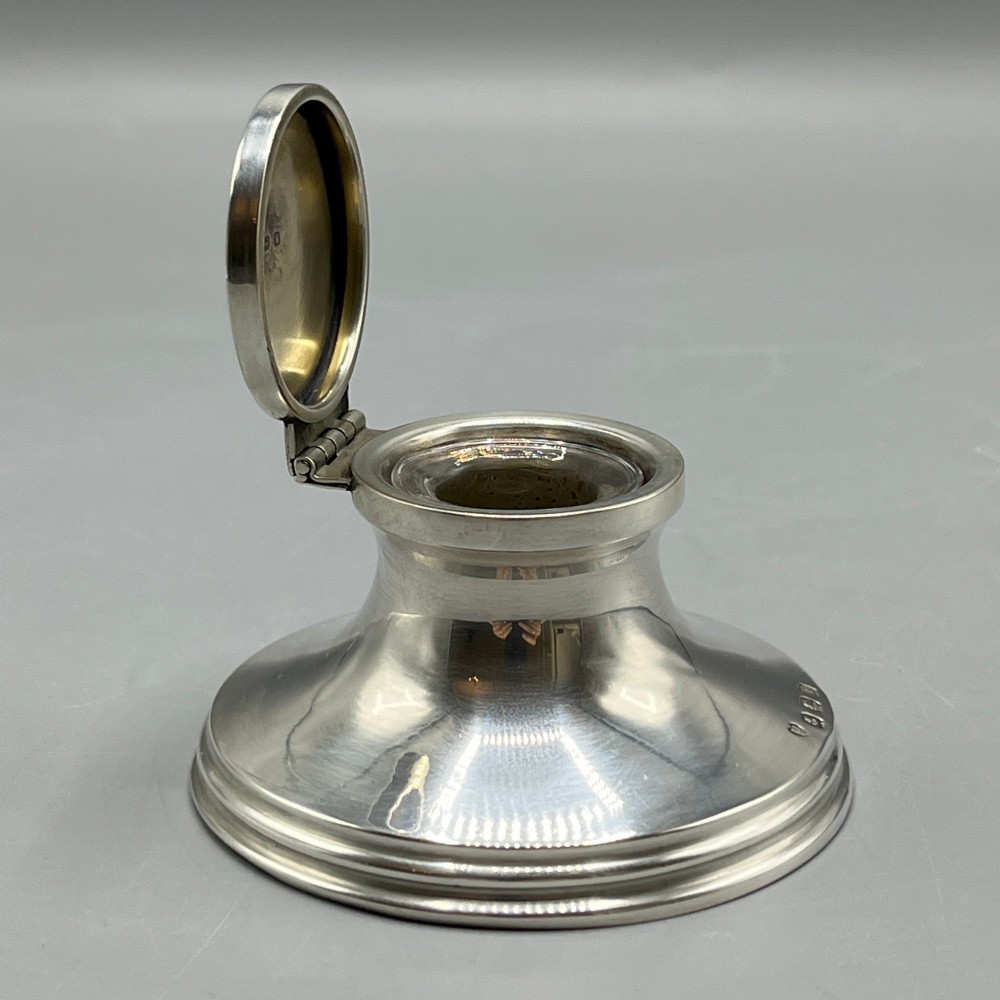An Art Deco sterling silver capstan inkwell featuring a smooth hinged lid, circular stepped base, and visible hallmarks. View IX