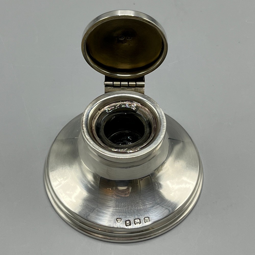 An Art Deco sterling silver capstan inkwell featuring a smooth hinged lid, circular stepped base, and visible hallmarks. View X
