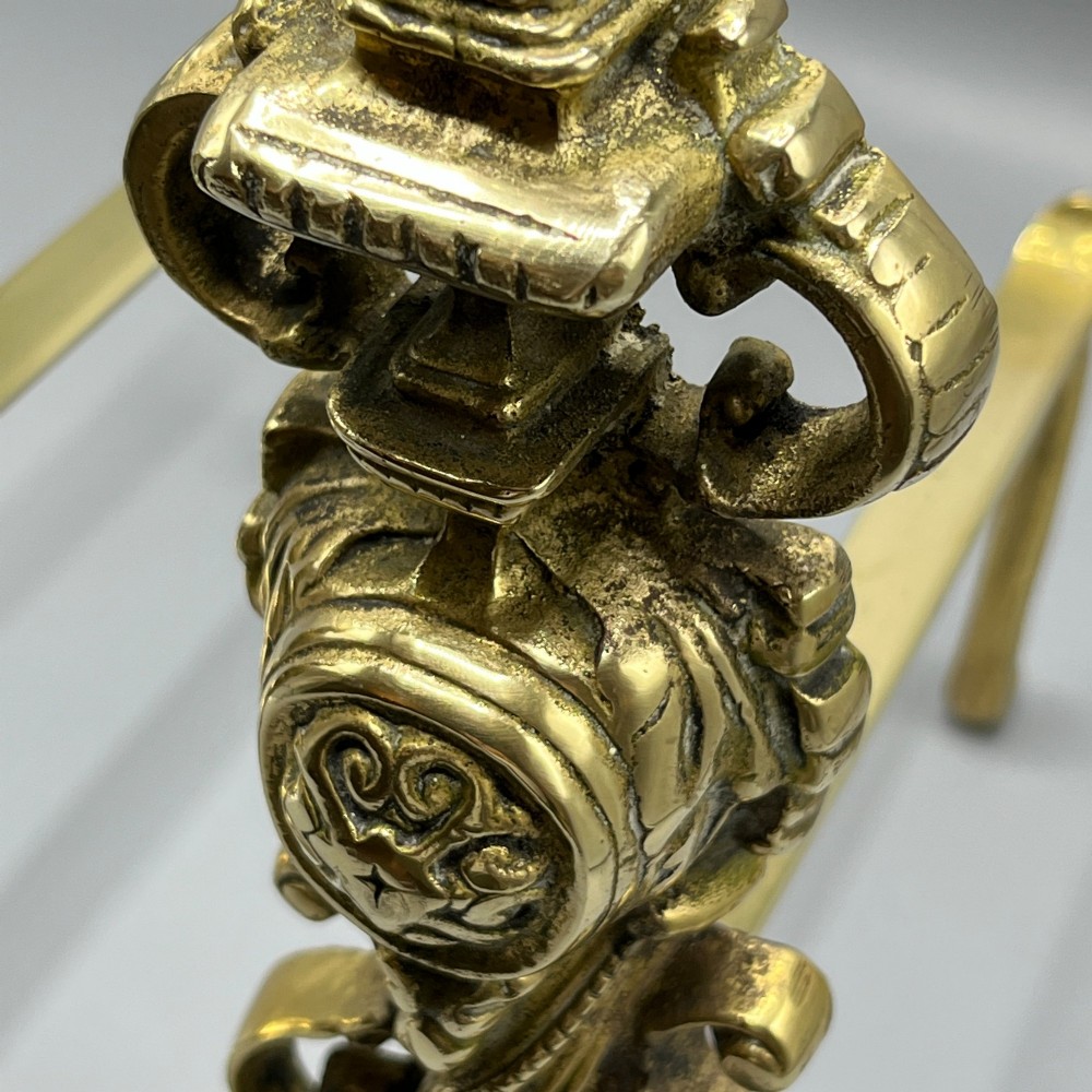 A pair of ornate Victorian solid brass fire dogs featuring finials, twisted columns, medallion details, and arched scrolled feet against a grey backdrop. View XI