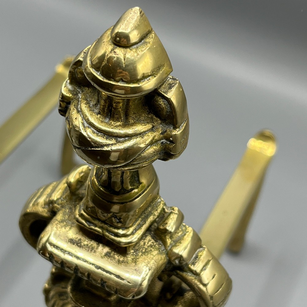 A pair of ornate Victorian solid brass fire dogs featuring finials, twisted columns, medallion details, and arched scrolled feet against a grey backdrop. View XII