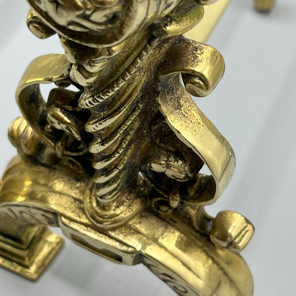 A pair of ornate Victorian solid brass fire dogs featuring finials, twisted columns, medallion details, and arched scrolled feet against a grey backdrop. View XIII