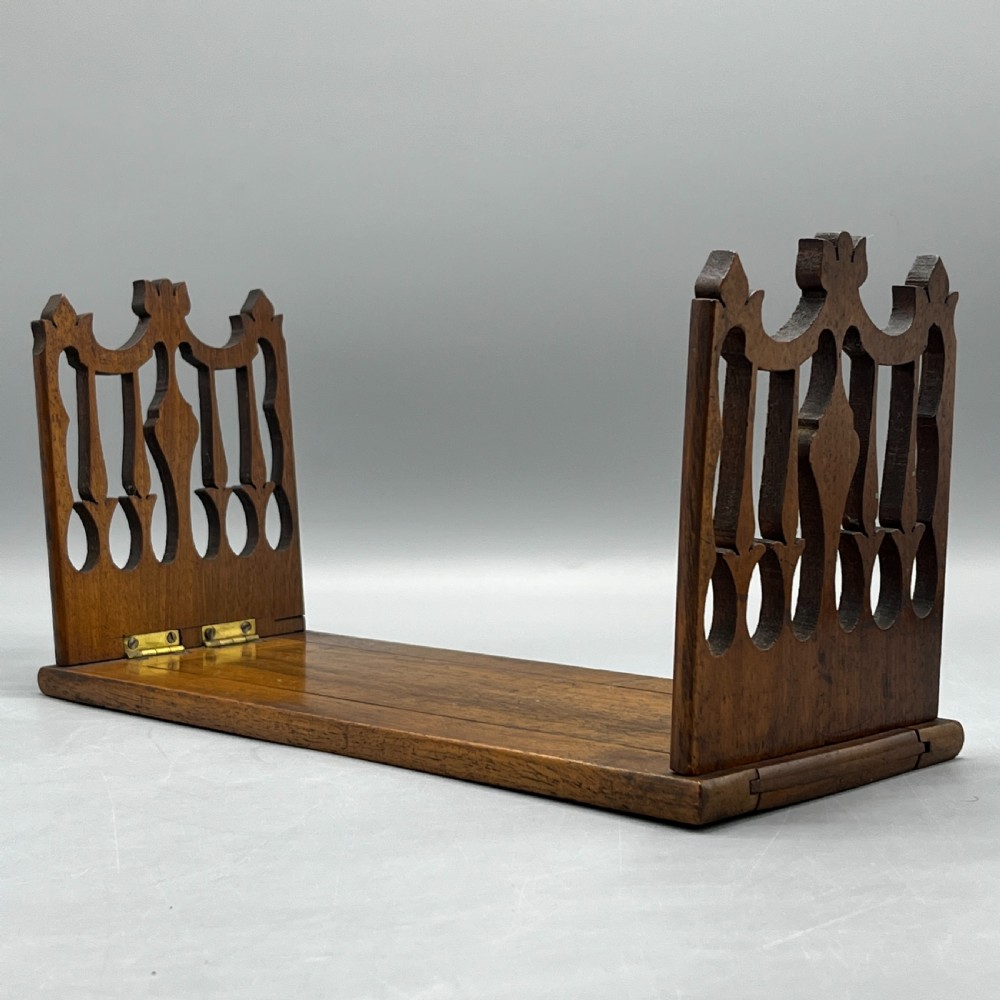 An Edwardian wooden extending book slide featuring carved pierced fretwork ends attached with brass hinges to a smooth base. View II