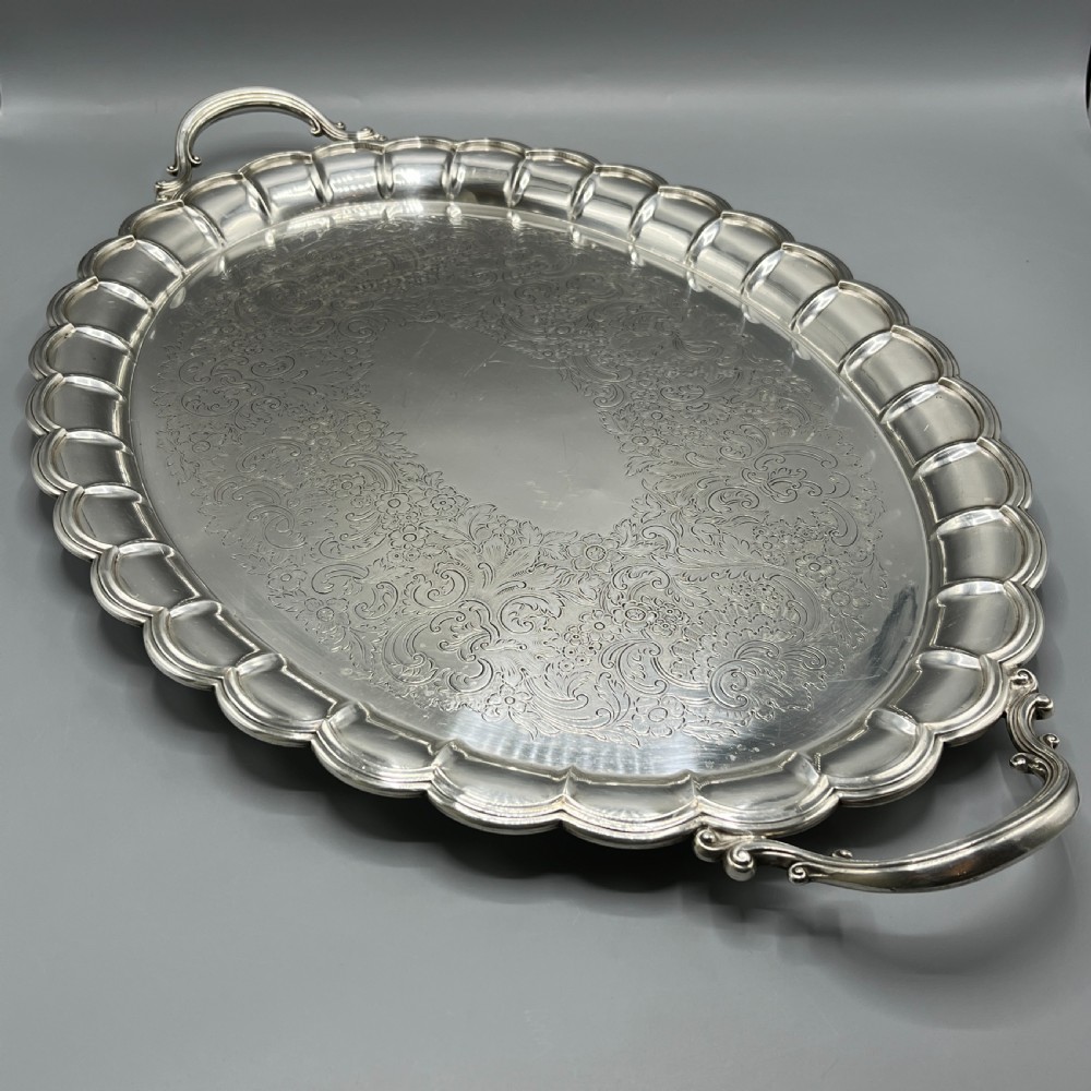 A large oval silver plated serving tray featuring twin scroll handles, a scalloped rim, and chased foliage patterns across the flat interior. View II
