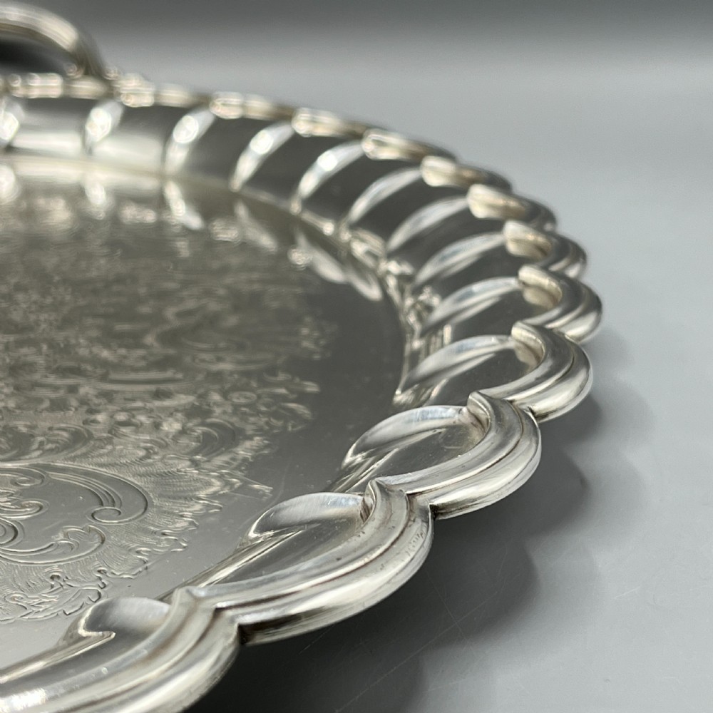 A large oval silver plated serving tray featuring twin scroll handles, a scalloped rim, and chased foliage patterns across the flat interior. View IV