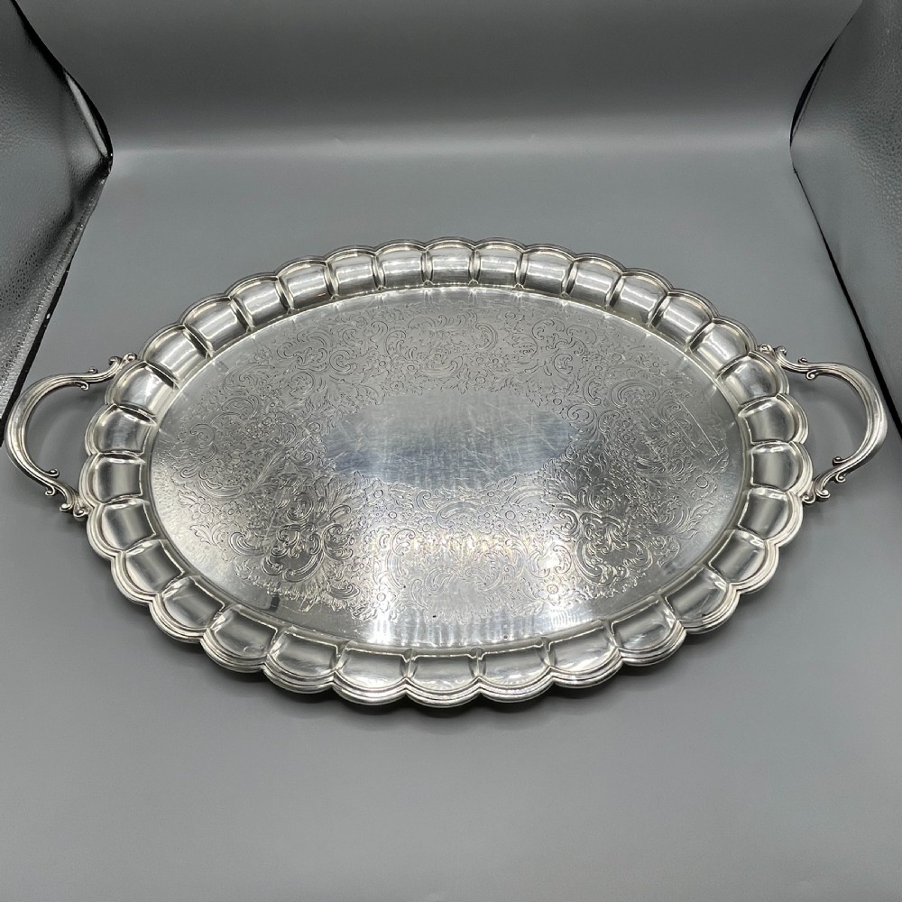 A large oval silver plated serving tray featuring twin scroll handles, a scalloped rim, and chased foliage patterns across the flat interior. View V